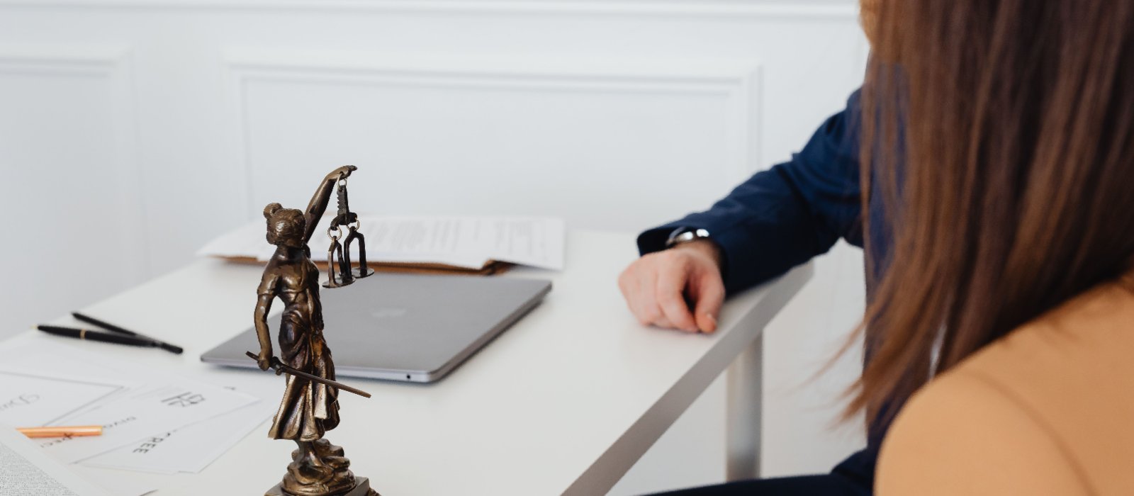 A client meeting her adviser across an office table, with a statuette of justice in the foreground